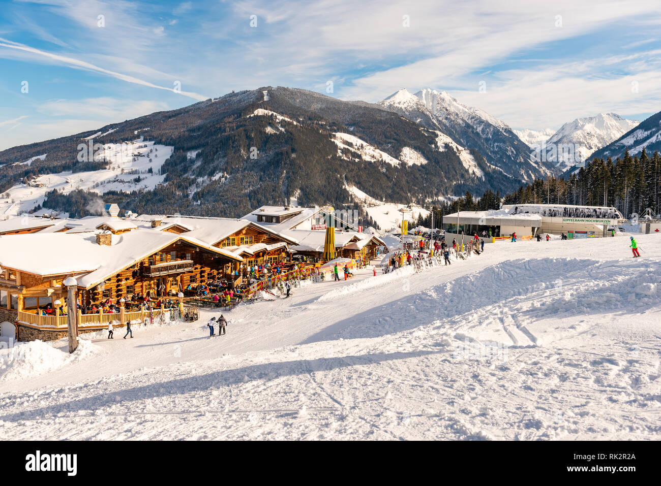 Ristorante Alpino pieno di sciatori, snowboarder e tobogganers sulla giornata di sole. Sullo sfondo la gondola Hochwurzen stazione di sci, montagne innevate. Foto Stock