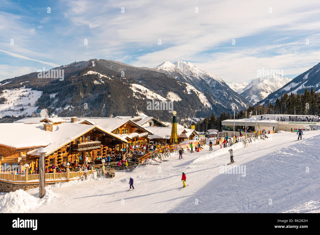 Ristorante Alpino pieno di sciatori, snowboarder e tobogganers sulla giornata di sole. Sullo sfondo la gondola Hochwurzen stazione di sci, montagne innevate. Foto Stock