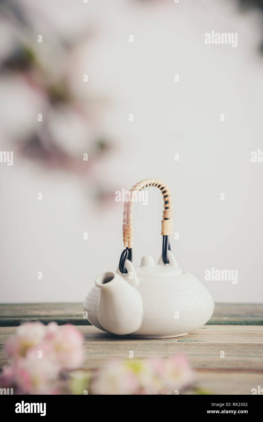 Teiera in bianco e fiori sakura sul tavolo di legno contro il muro bianco, il fuoco selettivo, spazio di copia Foto Stock