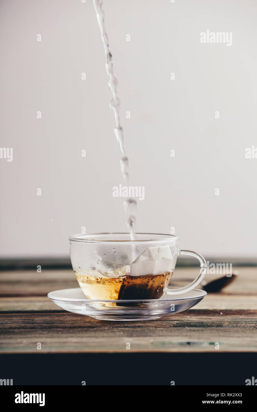 Versando acqua calda nel bicchiere di vetro con un sacchetto da tè, composizione verticale Foto Stock