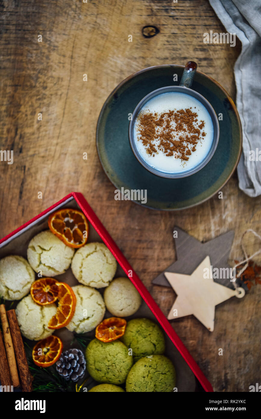 Una tazza di salep turco guarnita con cannella in polvere fotografata su uno sfondo di legno. Accompagnata da una scatola piena di cookies, bastoncini di cannella e o Foto Stock