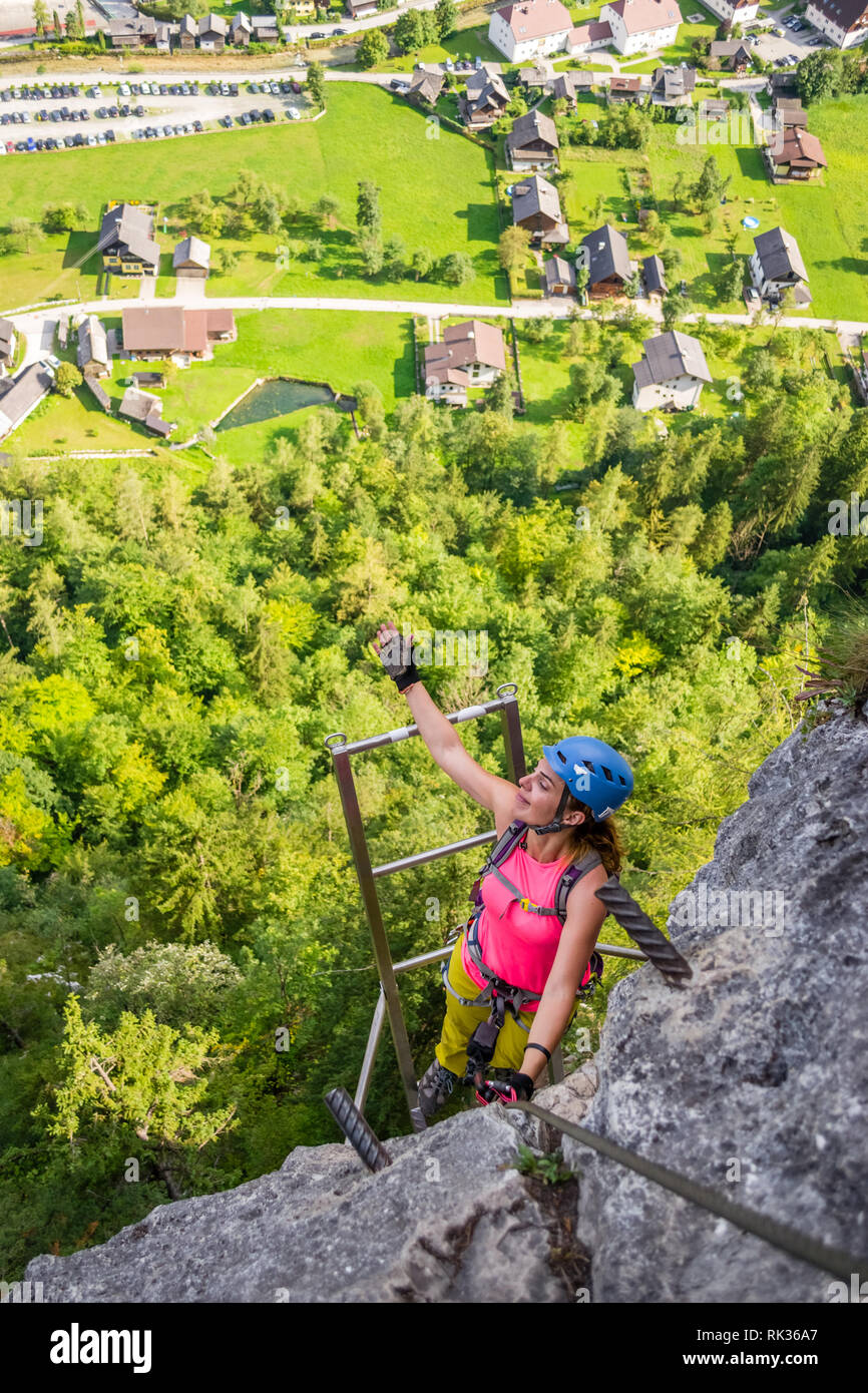 Felice giovane donna che salta una scala in ferro ferrata via 'Echernwand', sopra Hallstatt, Austria, durante un'escursione estiva Foto Stock