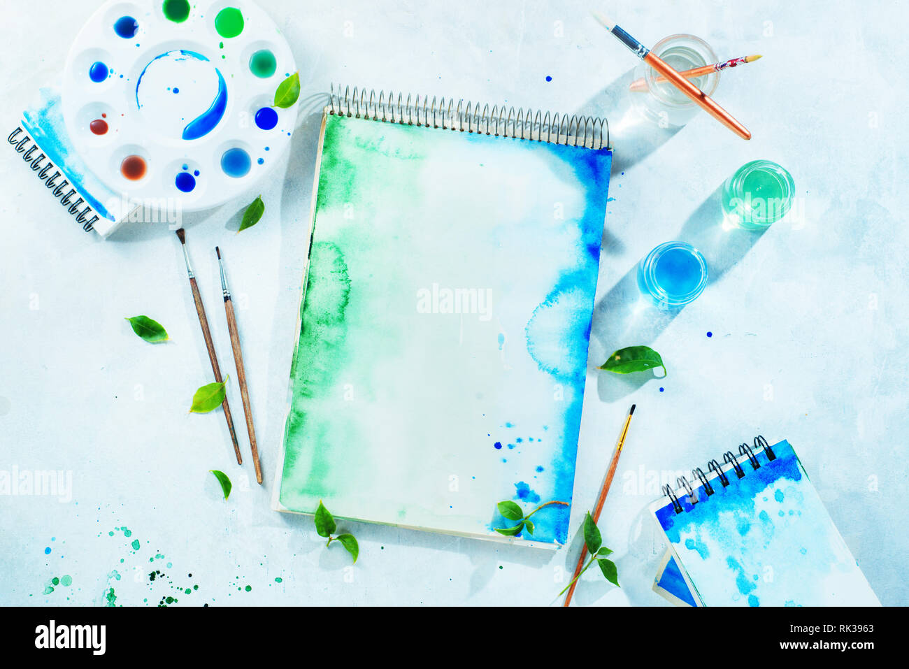 Molla di disegno concetto con gli strumenti dell'artista, il verde e il blu album da disegno ad acquerello, i pennelli e la tavolozza dei colori su uno sfondo luminoso con spazio di copia Foto Stock