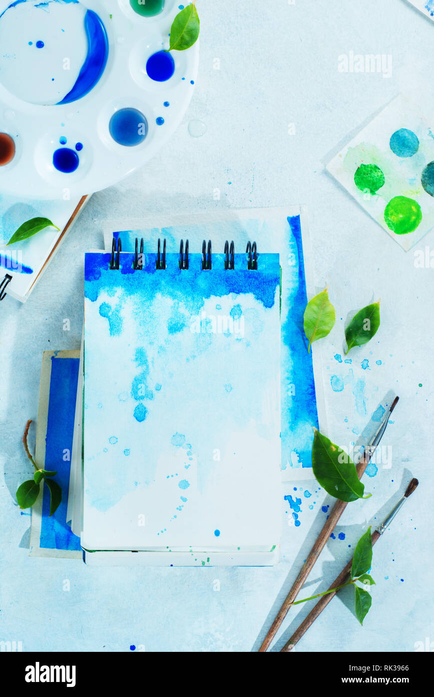 Molla di disegno concetto con gli strumenti dell'artista, il verde e il blu album da disegno ad acquerello, i pennelli e la tavolozza dei colori su uno sfondo luminoso con spazio di copia Foto Stock