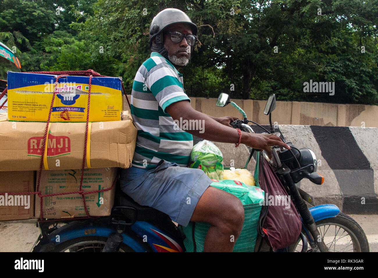 Un uomo con gli occhiali e il suo shopping sul retro della sua moto a Chennai, India meridionale Foto Stock