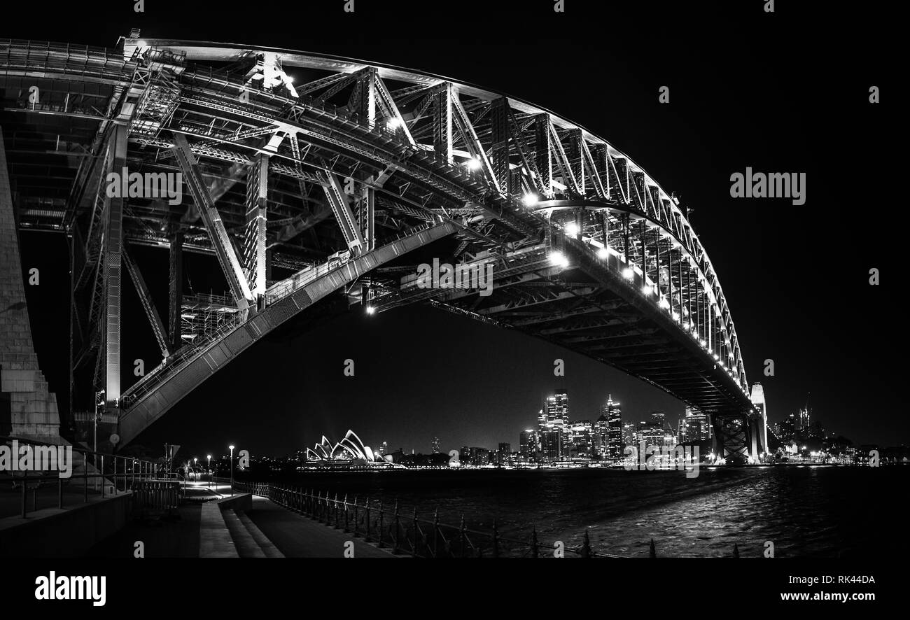 Sul lato est del Ponte del Porto di Sydney a nihgt con luminoso riflesso dalle acque sfocata del porto Foto Stock