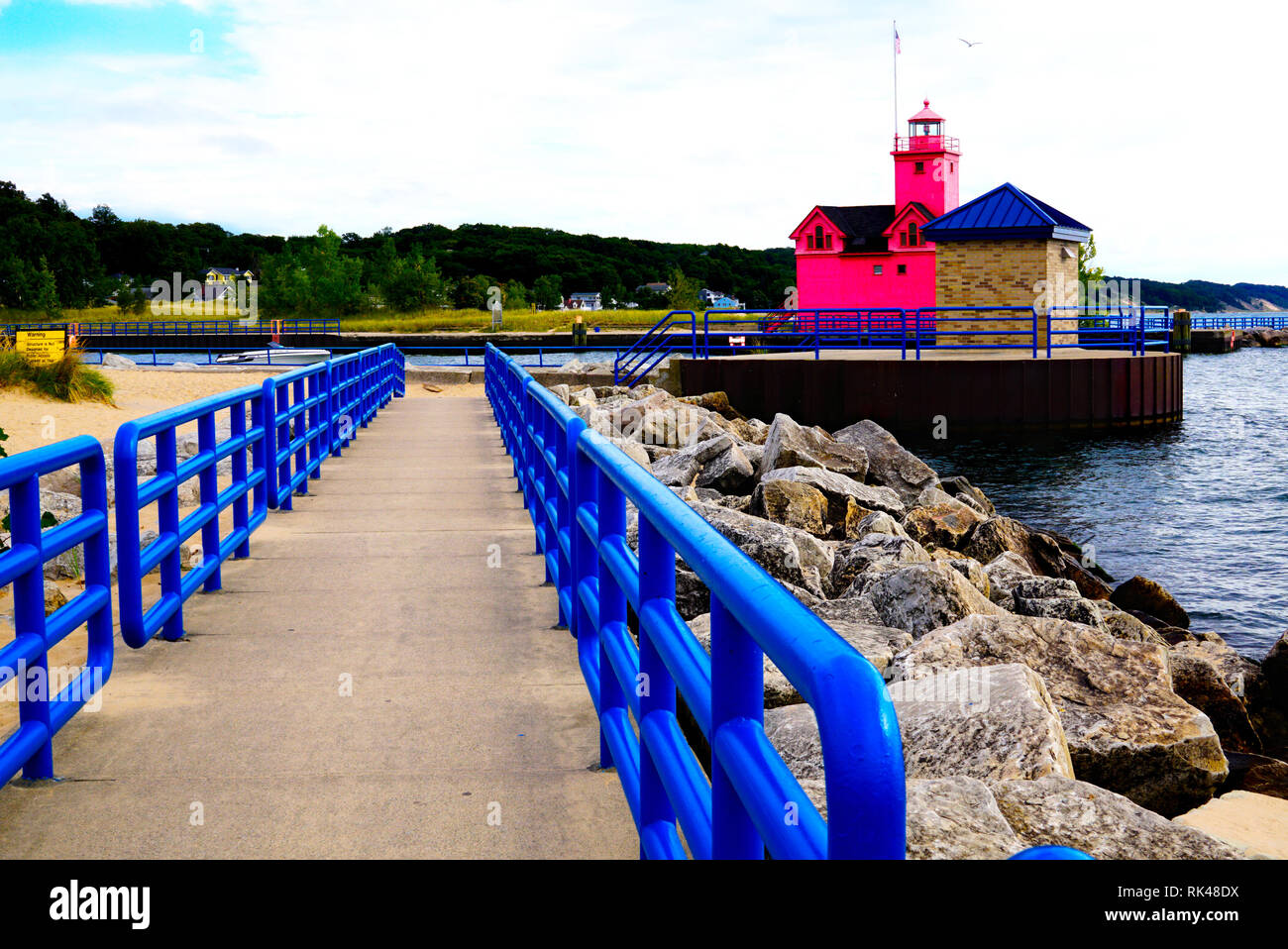 Holland Porto Grande luce rossa. Il molo con un blu brillante recinzione in prospettiva sulle rive del lago Michigan. Grossi massi vicino all'acqua. Albero verde Foto Stock