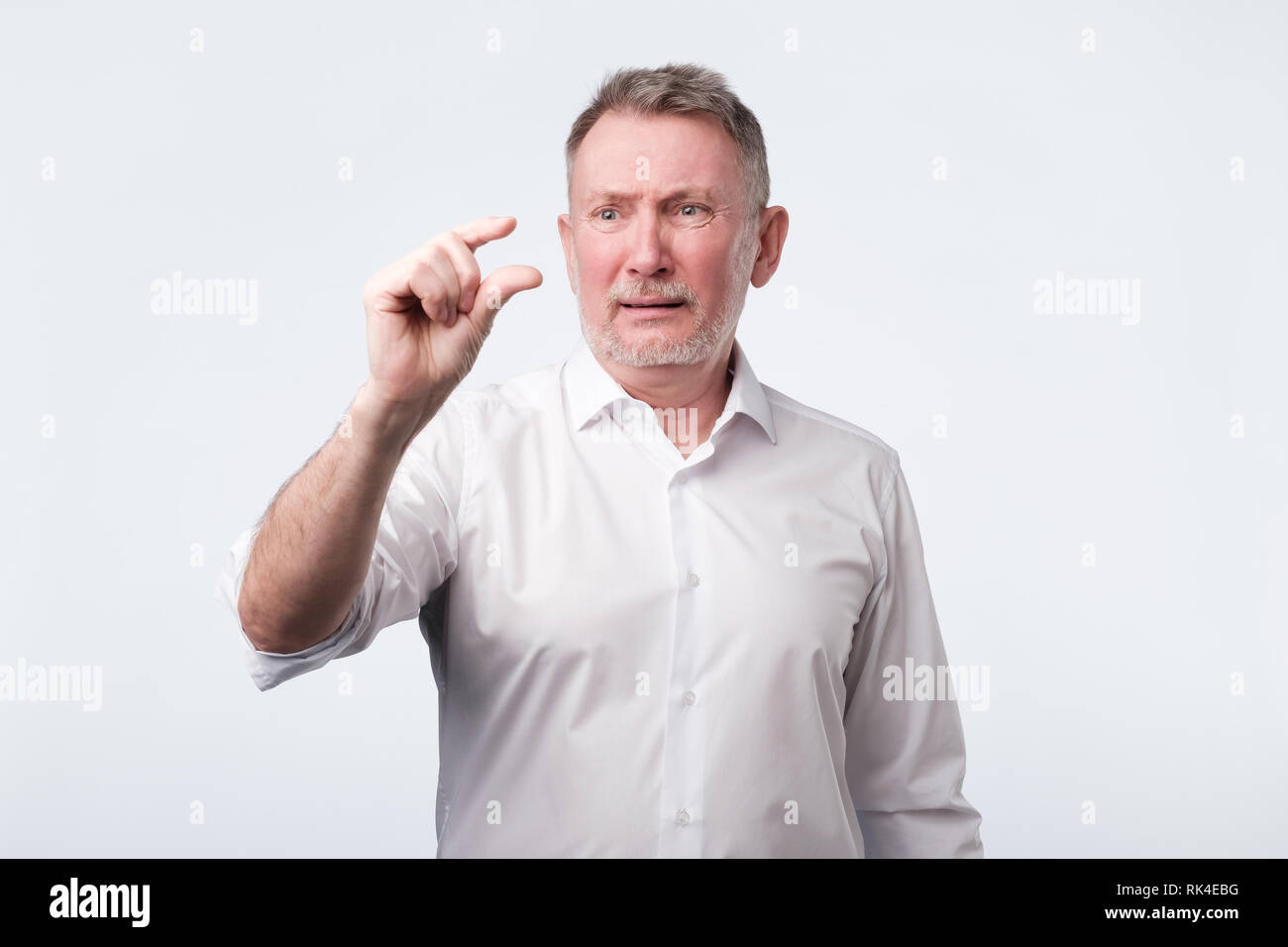 Senior uomo mostra un qualcosa di poco con la mano, dimostra un piccolo prestito. Foto Stock