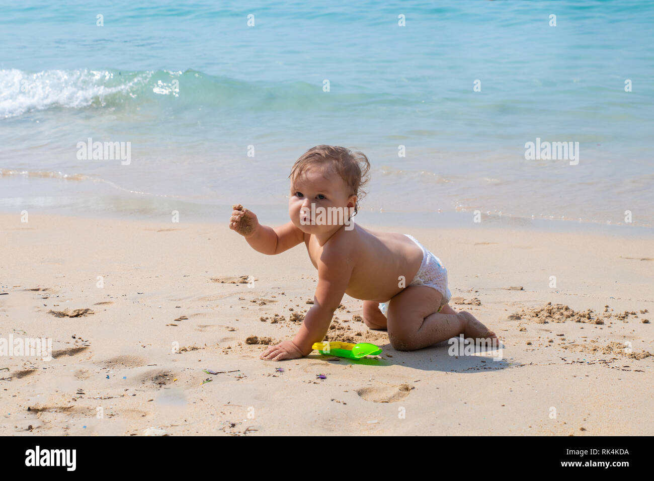 Bambino felice giocando in estate sul blu del mare.Baby crawl sulla spiaggia e gioca con i giocattoli. Foto Stock
