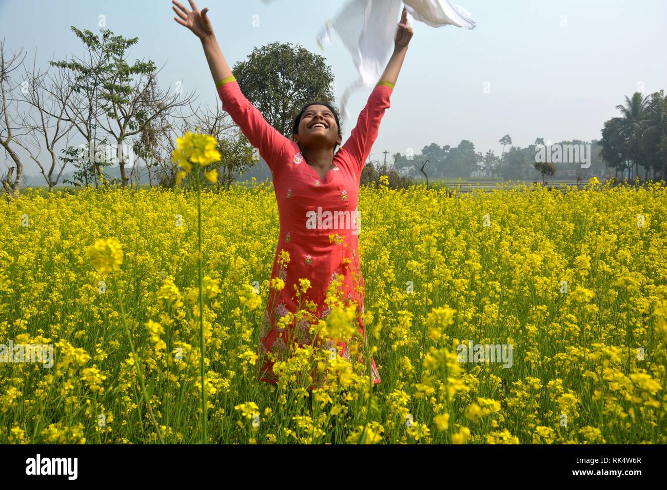 Una giovane ragazza saltando in gioia e battenti la sua dhupatta in aria in un giallo della colza, senape campo di fioritura in una giornata di sole Foto Stock