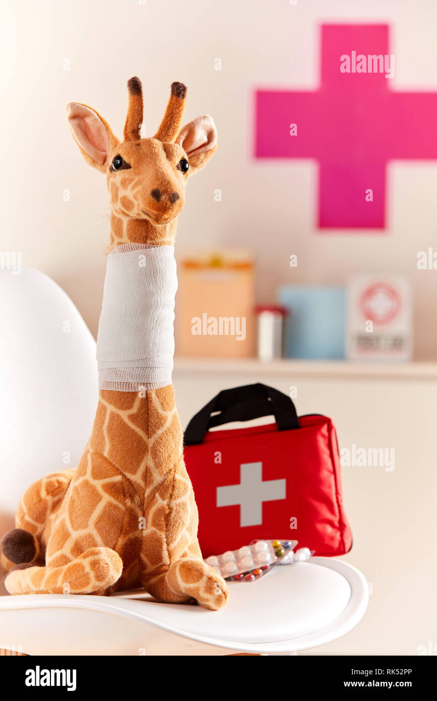 Toy giraffa con collo bendato in pediatra medici ufficio, accanto alla borsa con croce e medicina Foto Stock