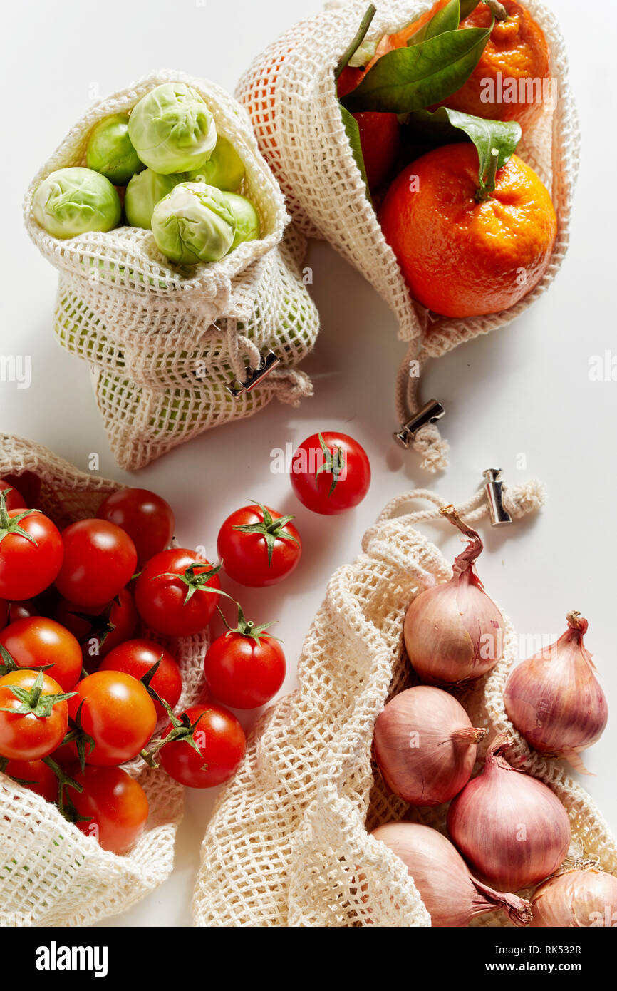 Vista superiore del fresco alimentari organici in rete riutilizzabili sacchetti. I pomodori, i cavoli di Bruxelles, la cipolla e le arance visto dal di sopra in close-up sulla superficie bianca Foto Stock