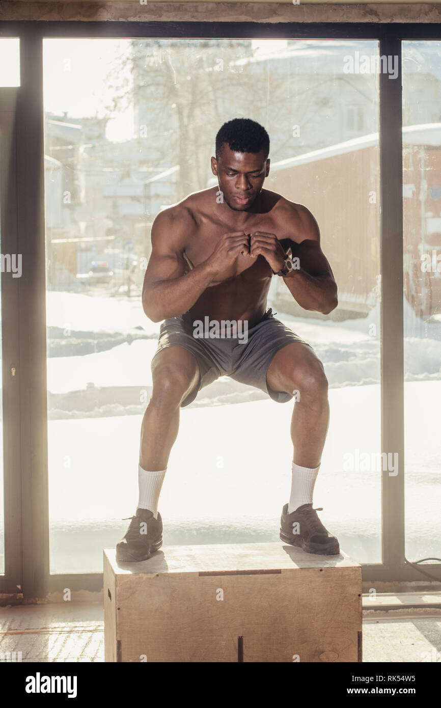 Bello forte uomo africano con torso nudo di saltare su un plyobox in un  cross training gym con grandi finestre panoramiche sullo sfondo Foto stock  - Alamy