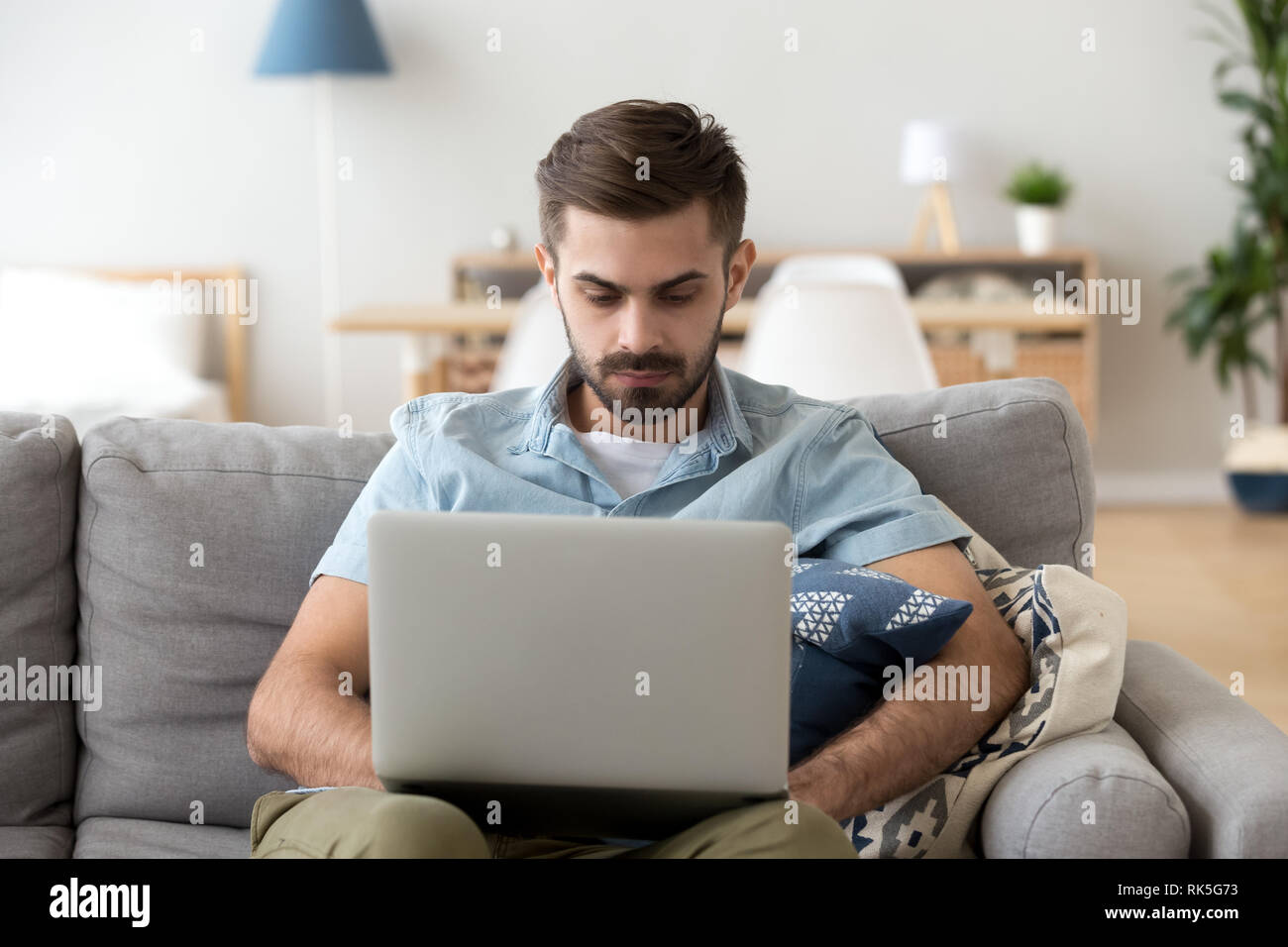 Uomo serio utilizzando laptop seduti sul divano a lavorare a casa Foto Stock