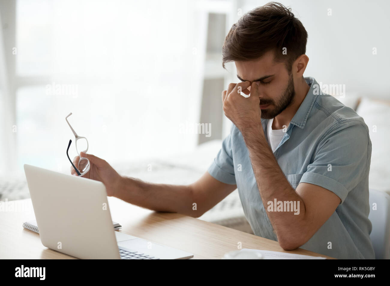 Sottolineato affaticato giovane uomo prendendo il largo bicchieri sensazione di affaticamento degli occhi mal di testa Foto Stock