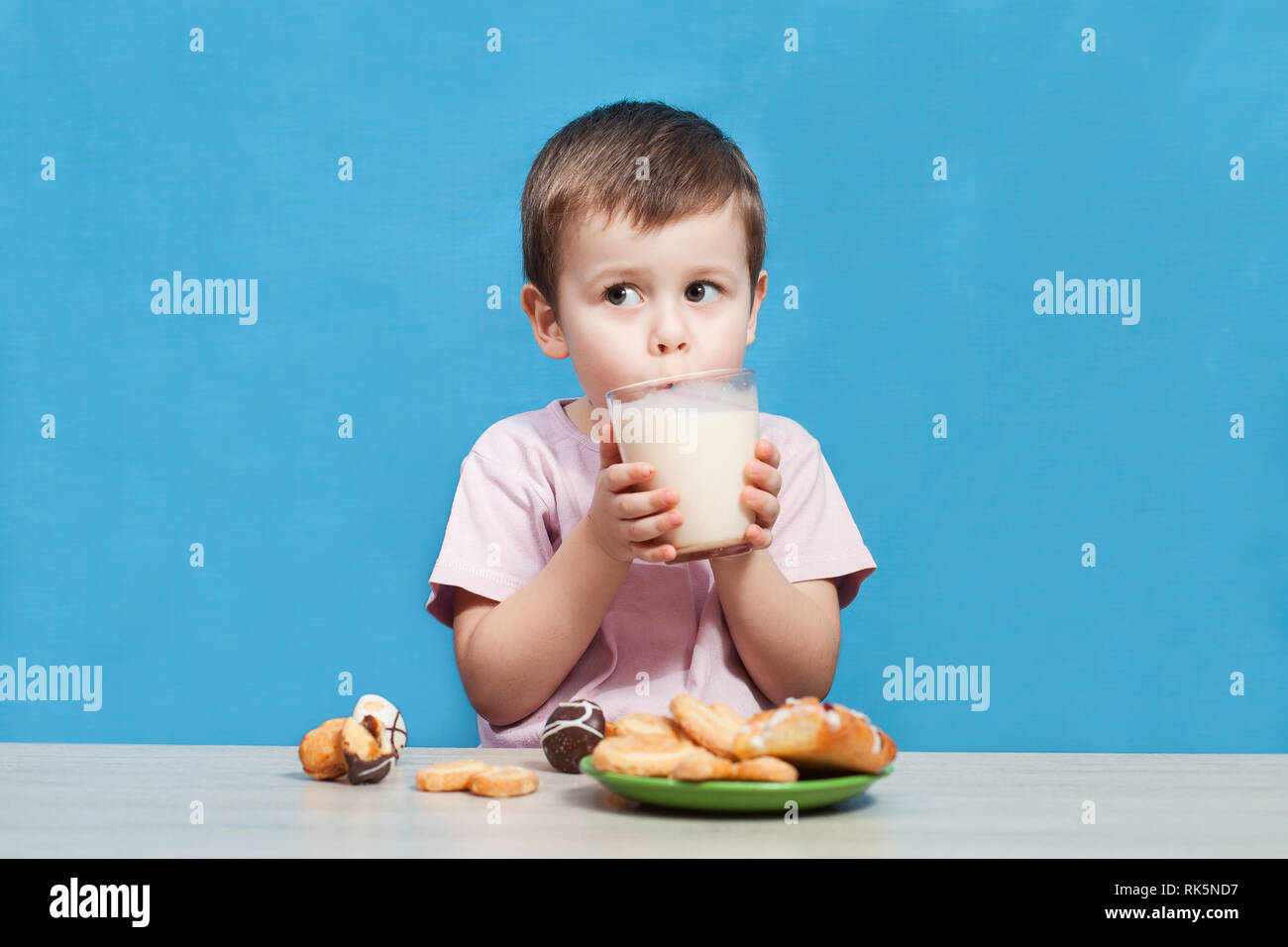 Carino piccolo ragazzo bere latte su sfondo blu. Foto Stock