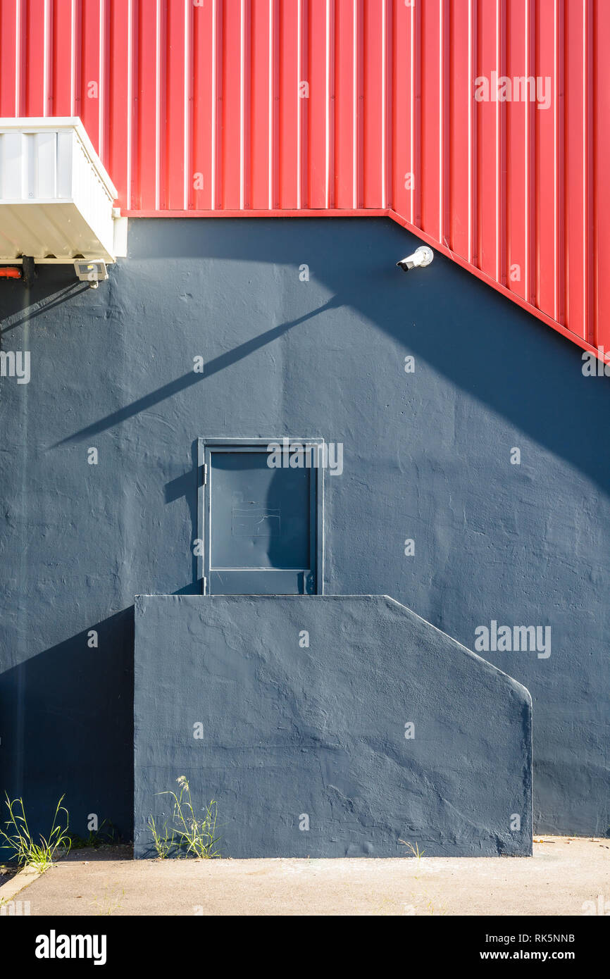 Una porta pedonale nella parete di un grande magazzino, alla sommità di una piccola scalinata, al di sotto di un rosso di ferro ondulato schierandosi con una videocamera di sicurezza. Foto Stock