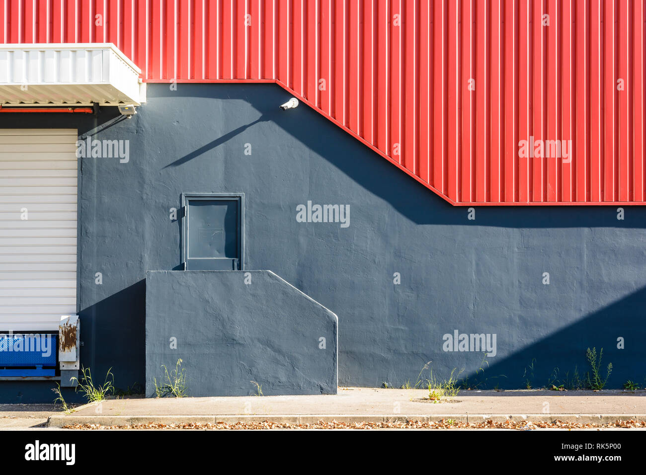 Una porta pedonale nella parete di un grande magazzino, alla sommità di una piccola scalinata, al di sotto di un rosso di ferro ondulato schierandosi con una videocamera di sicurezza. Foto Stock