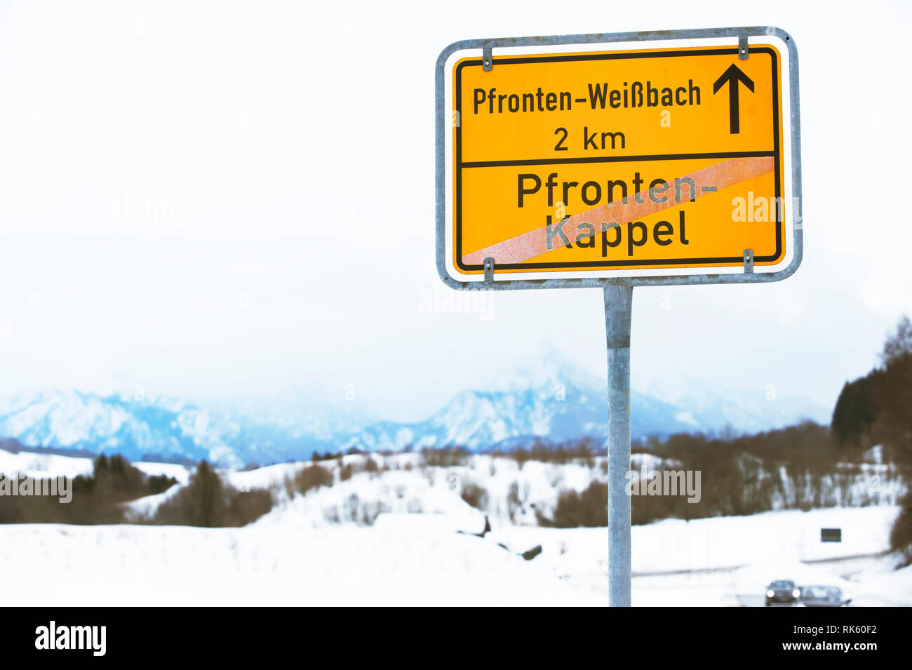 Giallo segno di traffico locale con i nomi di città. Paesaggio invernale con le montagne sullo sfondo. Pfronten in Baviera, Germania. Foto Stock