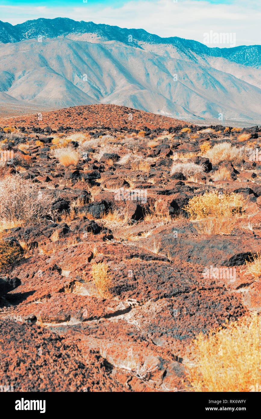 Roccia lavica paesaggio coperto di vegetazione rada crescente, aride montagne del deserto sotto nuvoloso cielo blu. Foto Stock