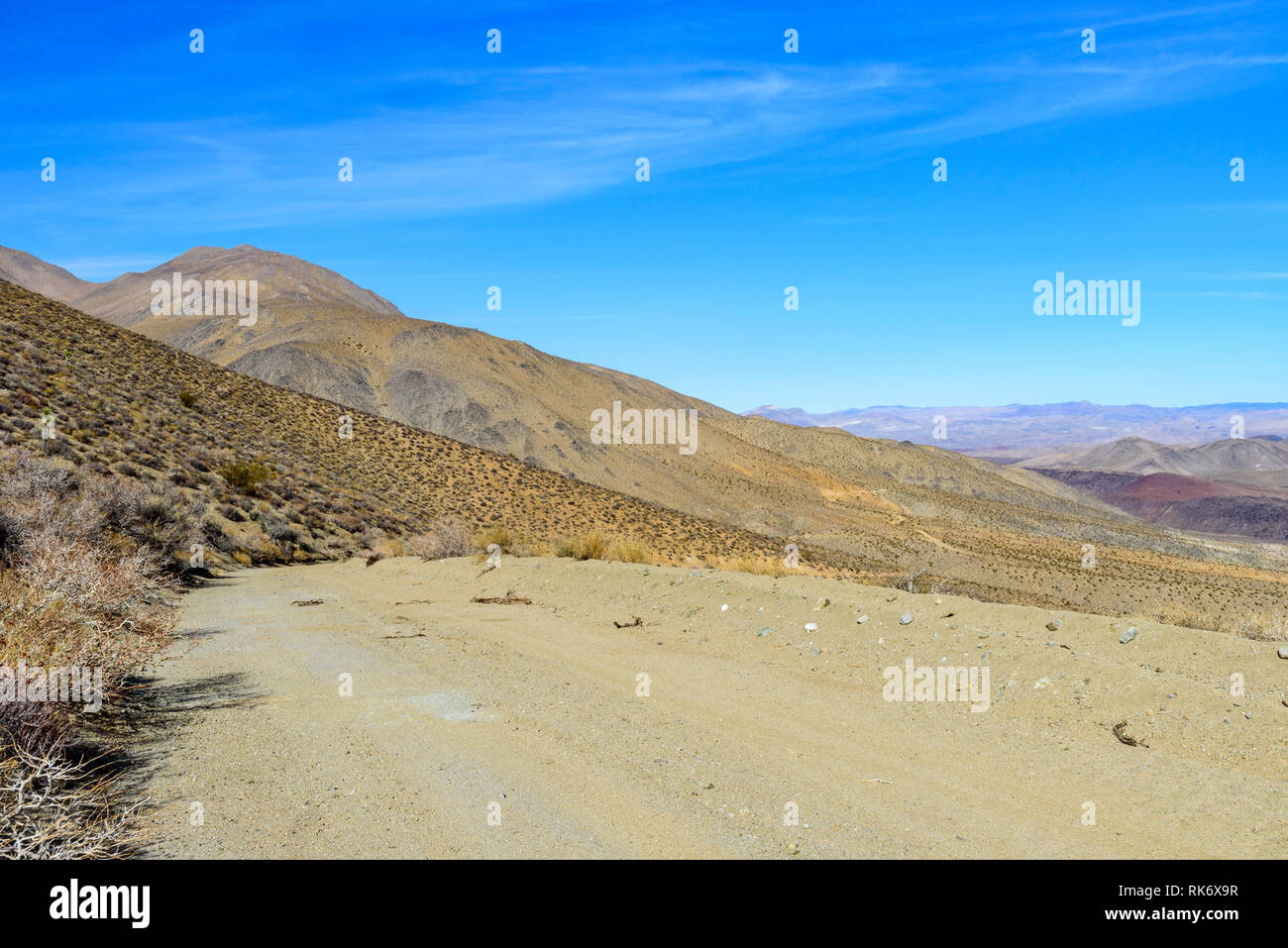 Deserto di strada sterrata che conduce verso montagne brulle sotto il luminoso cielo blu. Foto Stock