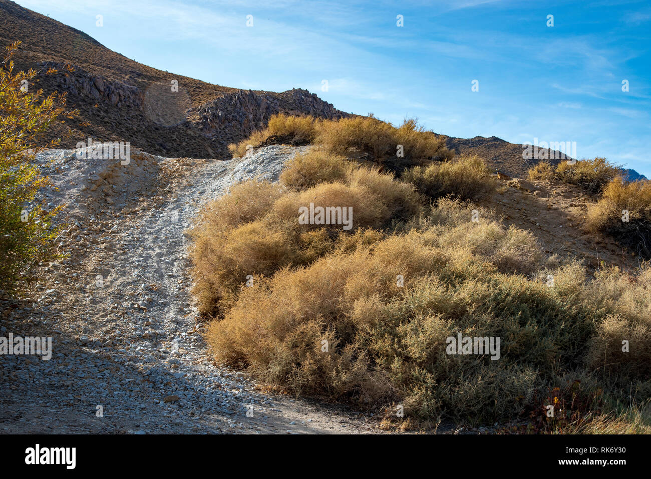 Stretta strada sterrata che conduce sulla collina ripida verso le montagne al di là sotto il luminoso cielo blu. Foto Stock