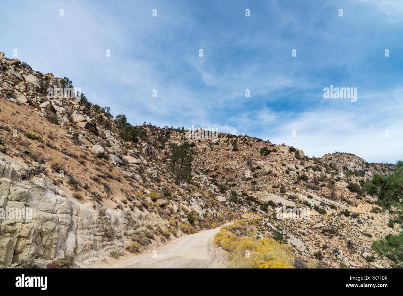 Strada sterrata che conduce attraverso delle montagne del deserto con la montagna sulla sinistra e scendere a destra sotto il cielo blu con nuvole. Foto Stock