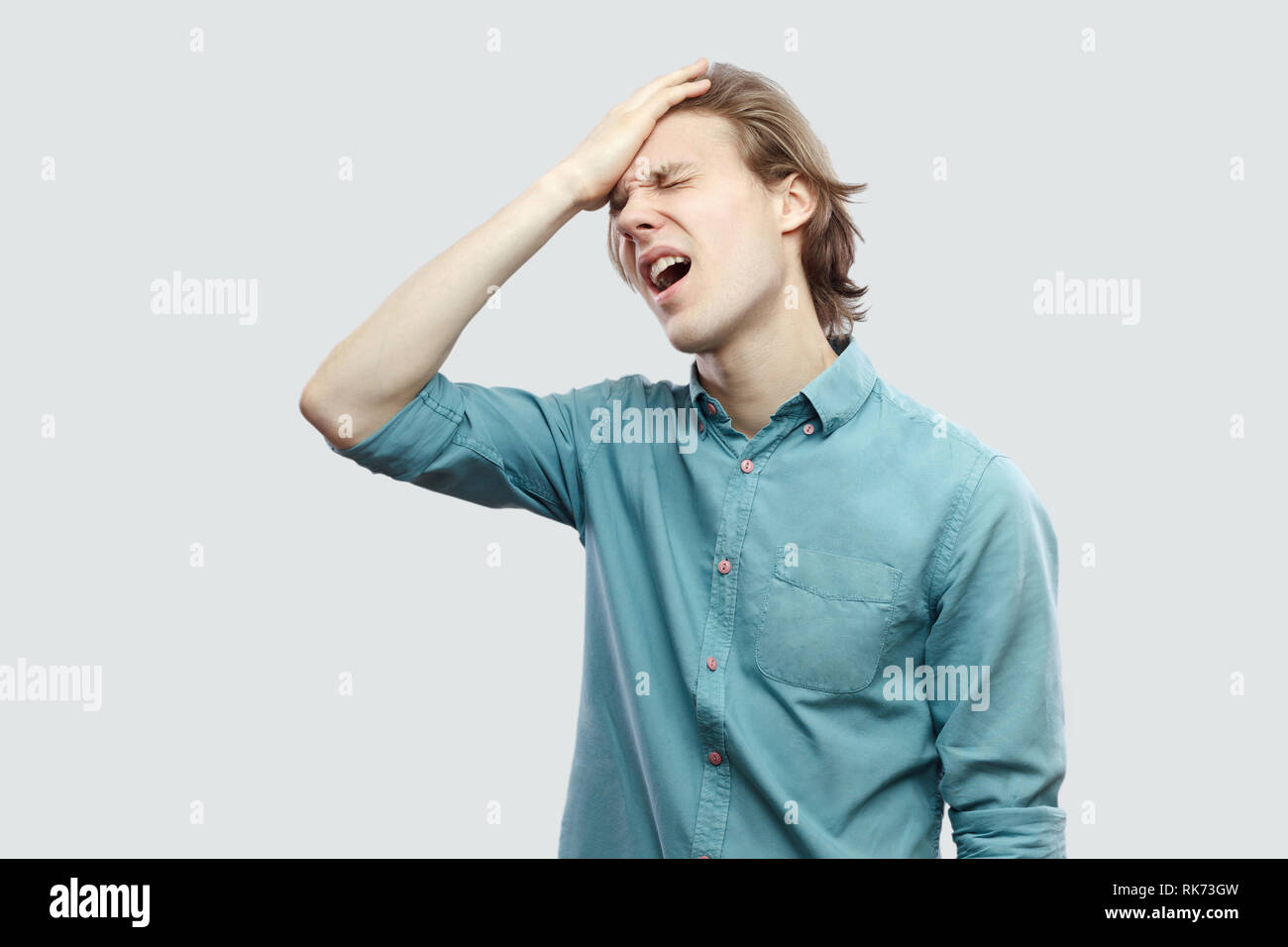 Egli ha perso tutto. Ritratto di triste bello capelli lunghi biondo giovane uomo in blu Camicia casual permanente e la triste perchè il suo errore di nuovo prigioniero al coperto Foto Stock