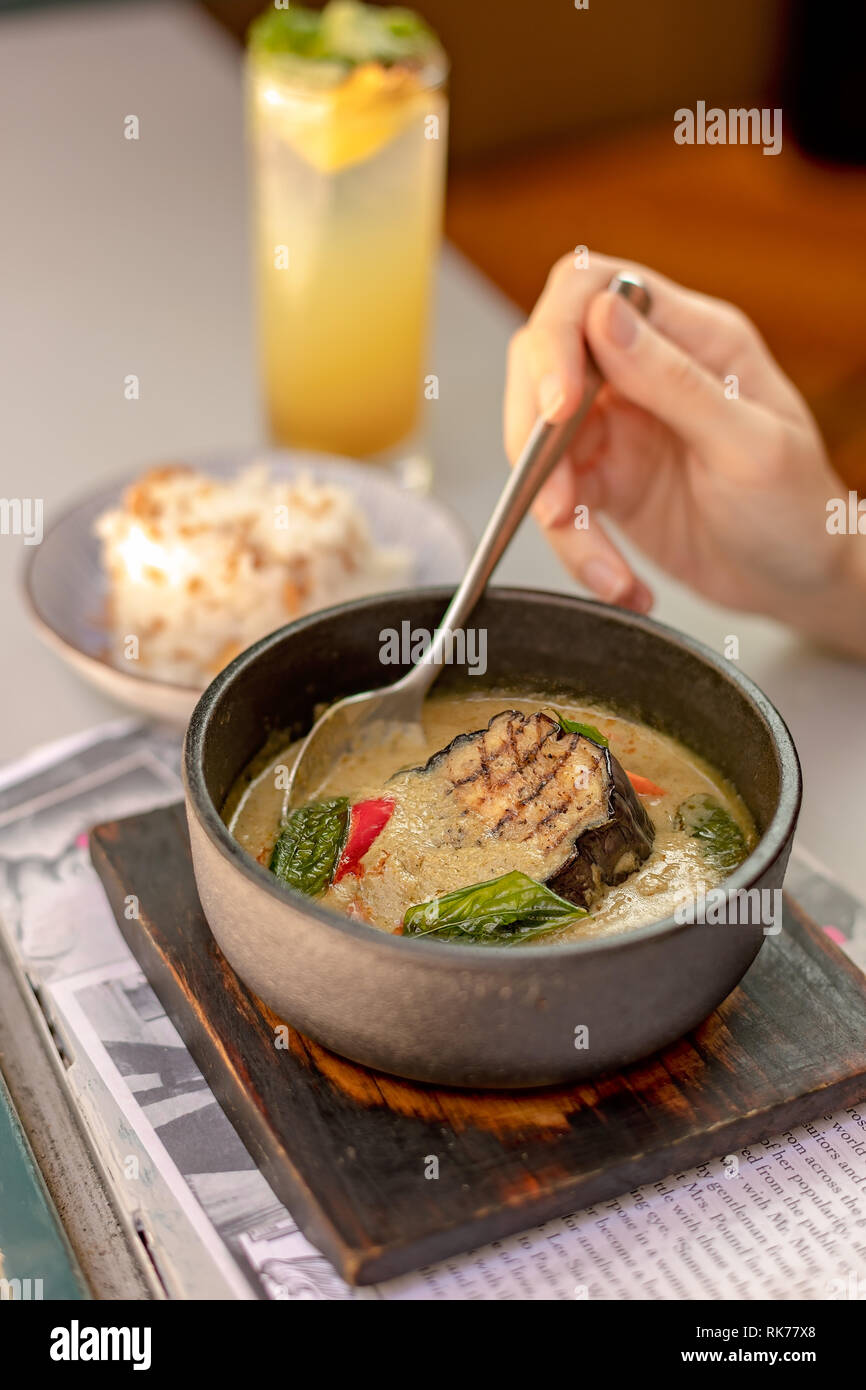 Mano tenendo un cucchiaio pronto a mangiare il delizioso vegetariano melanzane verde curry Foto Stock