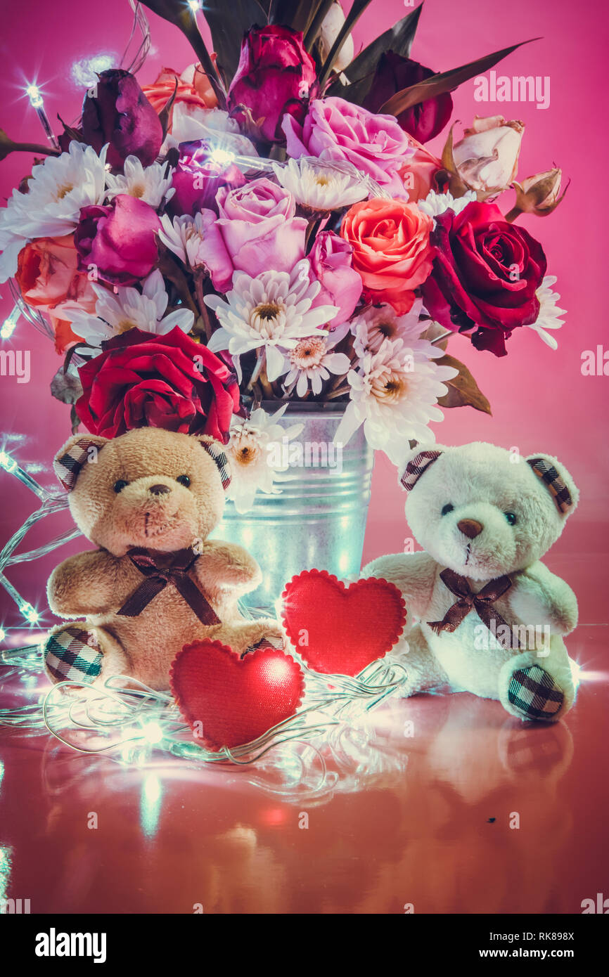 Coppia adorabile Orso e cuore rosso sito nelle vicinanze di vaso di bouquet di rose in alluminio benna su sfondo rosa. Il giorno di San Valentino del concetto. Foto Stock