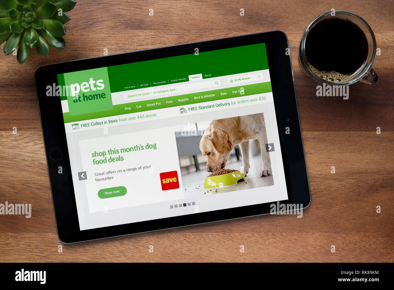 Il sito web di animali domestici in casa è visto su un tablet iPad, su di un tavolo di legno lungo con un caffè espresso e una pianta di casa (solo uso editoriale). Foto Stock