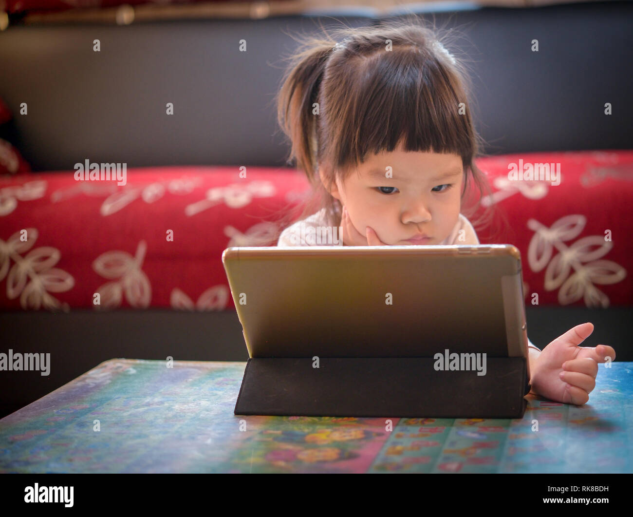 Bambino asiatico ragazza seduta a guardare il tablet in home Foto Stock