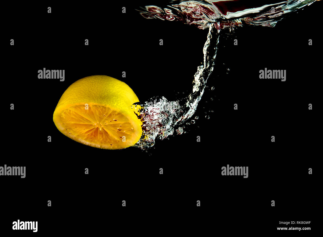 Mezzo limone cadere in acqua su sfondo nero Foto Stock