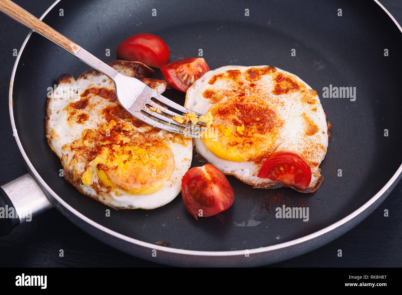 Uova fritte in padella con paprika affumicato e freschi pomodori ciliegia. Illuminazione naturale. Close up. Foto Stock