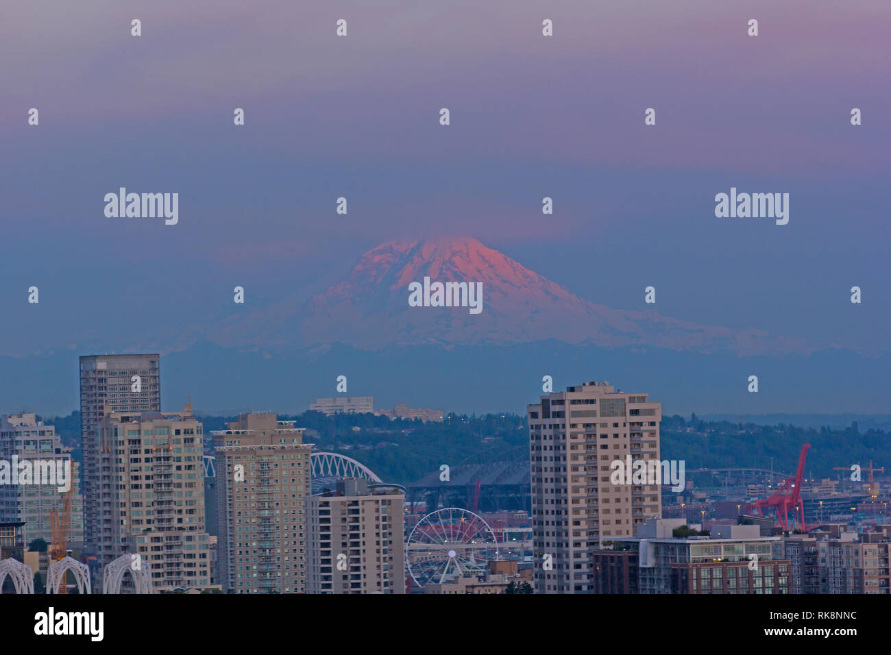 Famosa montagna in tinte pastello dei cieli è illuminata dalla luce del sole. Urban panorama di Seattle e il Monte Rainier sull orizzonte al tramonto, Washington, Stati Uniti d'America. Foto Stock