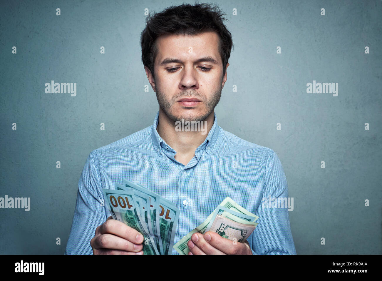 Ritratto di uomo caucasico in camicia conteggiare denaro sul muro grigio Sfondo. Business e concetto finanziario Foto Stock