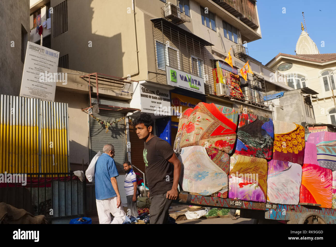 Un estrattore di camion di manovrare il suo carrello con balle di stoffa colorata attraverso i vicoli della business area Bhuleshwar, Mumbai, India Foto Stock