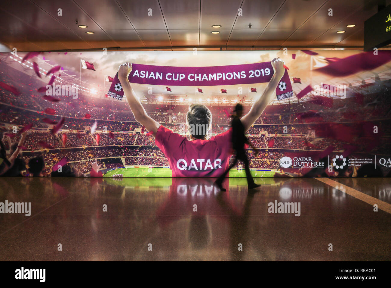 Doha in Qatar. Il 10 febbraio 2019. La gente a piedi passato un grande cartellone elettronico al Hamad dall'Aeroporto Internazionale di Doha celebrando il Qatar come 2019 Asian Champions Cup. Il Qatar sarà il paese ospitante per il 2022 World Cup Credito: amer ghazzal/Alamy Live News Foto Stock