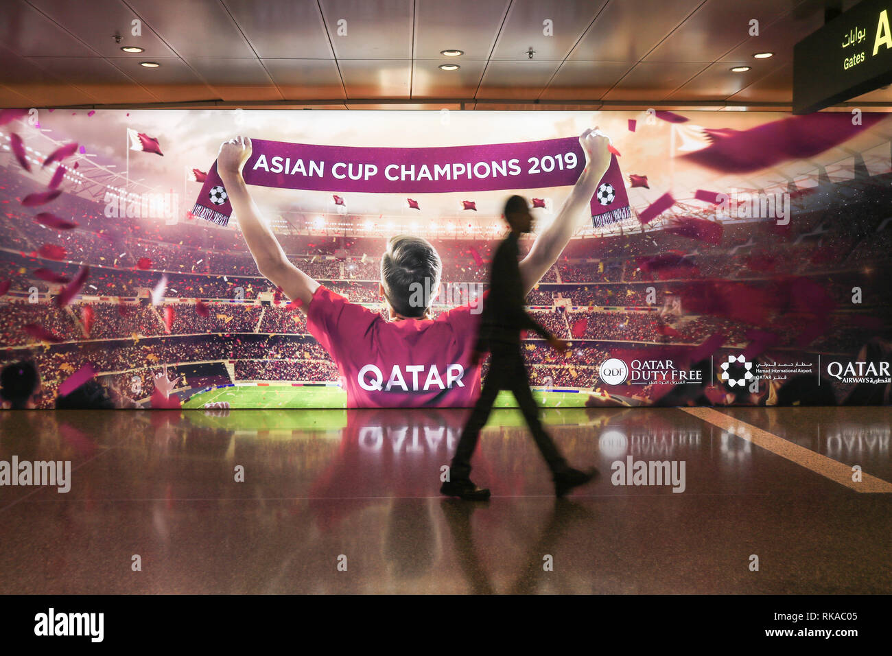 Doha in Qatar. Il 10 febbraio 2019. La gente a piedi passato un grande cartellone elettronico al Hamad dall'Aeroporto Internazionale di Doha celebrando il Qatar come 2019 Asian Champions Cup. Il Qatar sarà il paese ospitante per il 2022 World Cup Credito: amer ghazzal/Alamy Live News Foto Stock
