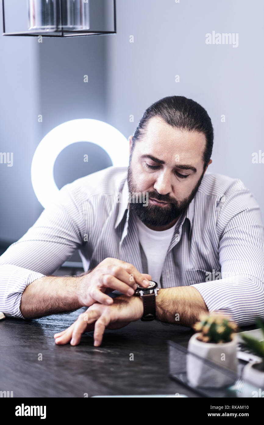 Dai capelli scuri uomo barbuto in una camicia a righe controllando il suo orologio Foto Stock