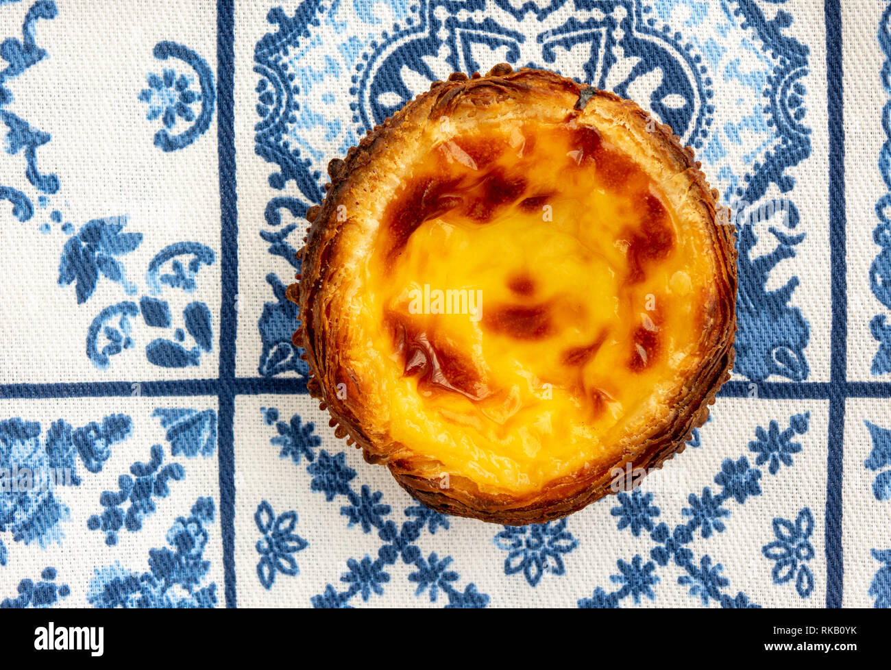 Un singolo Pastel de nata sul tradizionale blu e bianco piastrella Azulejo sfondo asciugamano Foto Stock