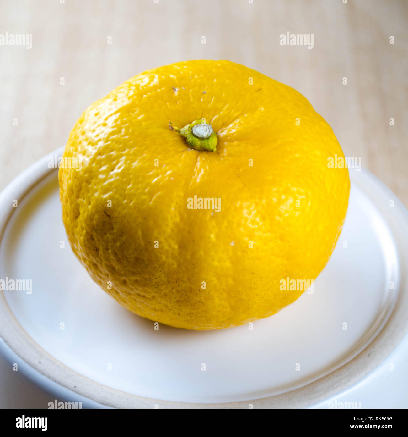 Yuzu frutta (un giapponese varietà di agrumi) su una piccola piastra bianca contro uno sfondo di legno Foto Stock