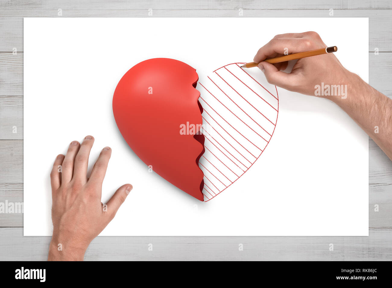 Vista da sopra delle mani dell'uomo su un banco di disegno con una matita  la seconda metà di quello rotto cuore rosso giacenti su un foglio bianco di  carta Foto stock -