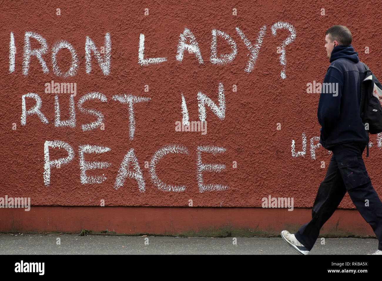 Un pedone passato passeggiate graffiti che recita "signora di ferro? Ruggine in pace" riferendosi all'ex primo ministro britannico Margaret Thatcher nella parte occidentale di Belfast, Irlanda del Nord il 9 aprile, 2013 Un giorno successivo Thatcher della morte. La Gran Bretagna era profondamente divisa sulla eredità dell ex primo ministro Margaret Thatcher come i preparativi per il grand funerale la prossima settimana della donna noto in tutto il mondo come la "signora di ferro". Foto/Paolo McErlane Foto Stock