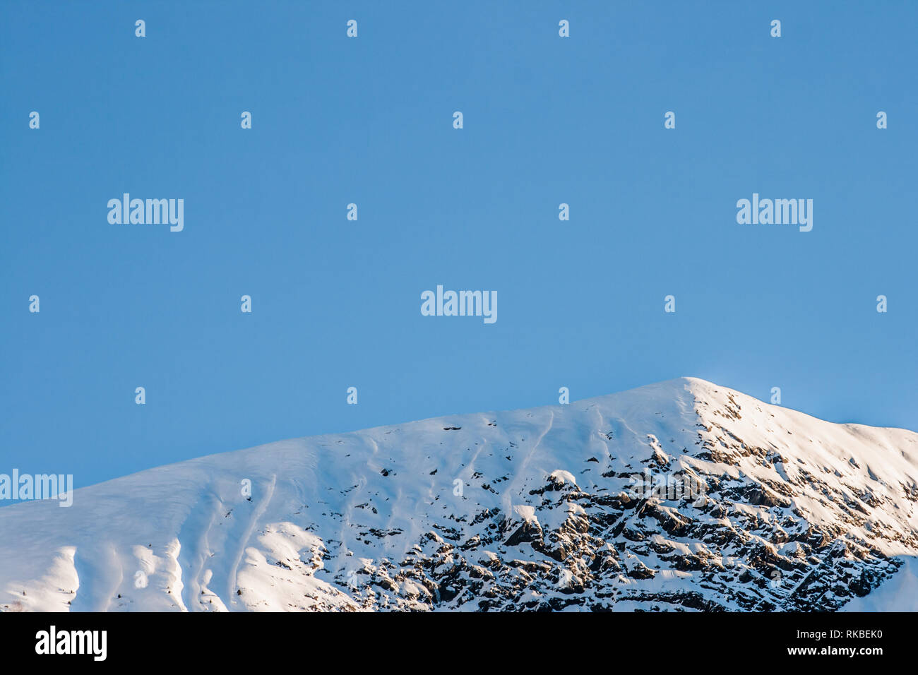 In alto di neve soffice, contrastato Rocky Mountain contro un luminoso cielo blu con abbondanza di spazio di copia. Minimalista stagione invernale shot. Foto Stock