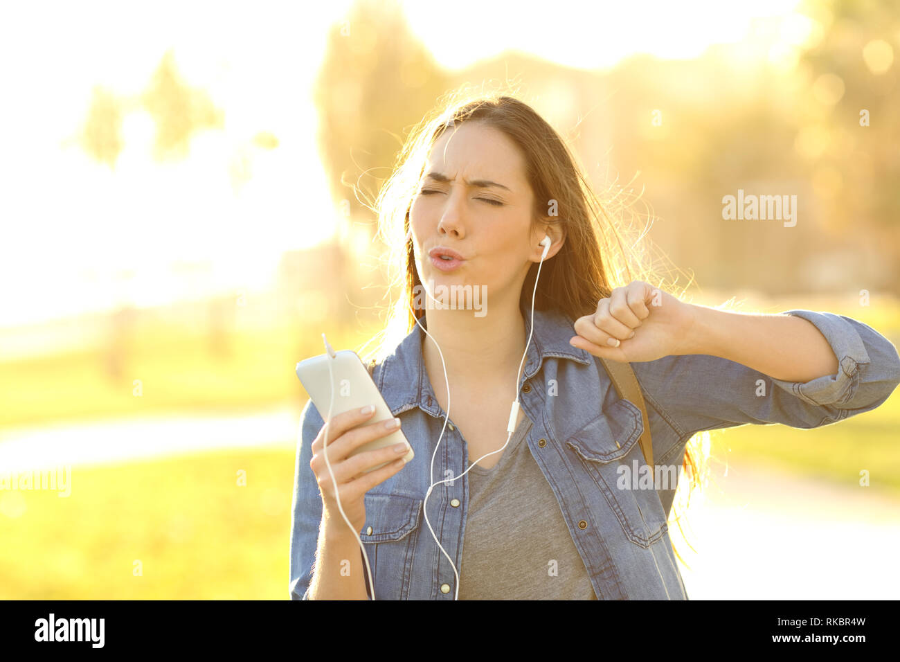 Donna felice godendo ascoltando la musica e il canto in strada al tramonto Foto Stock