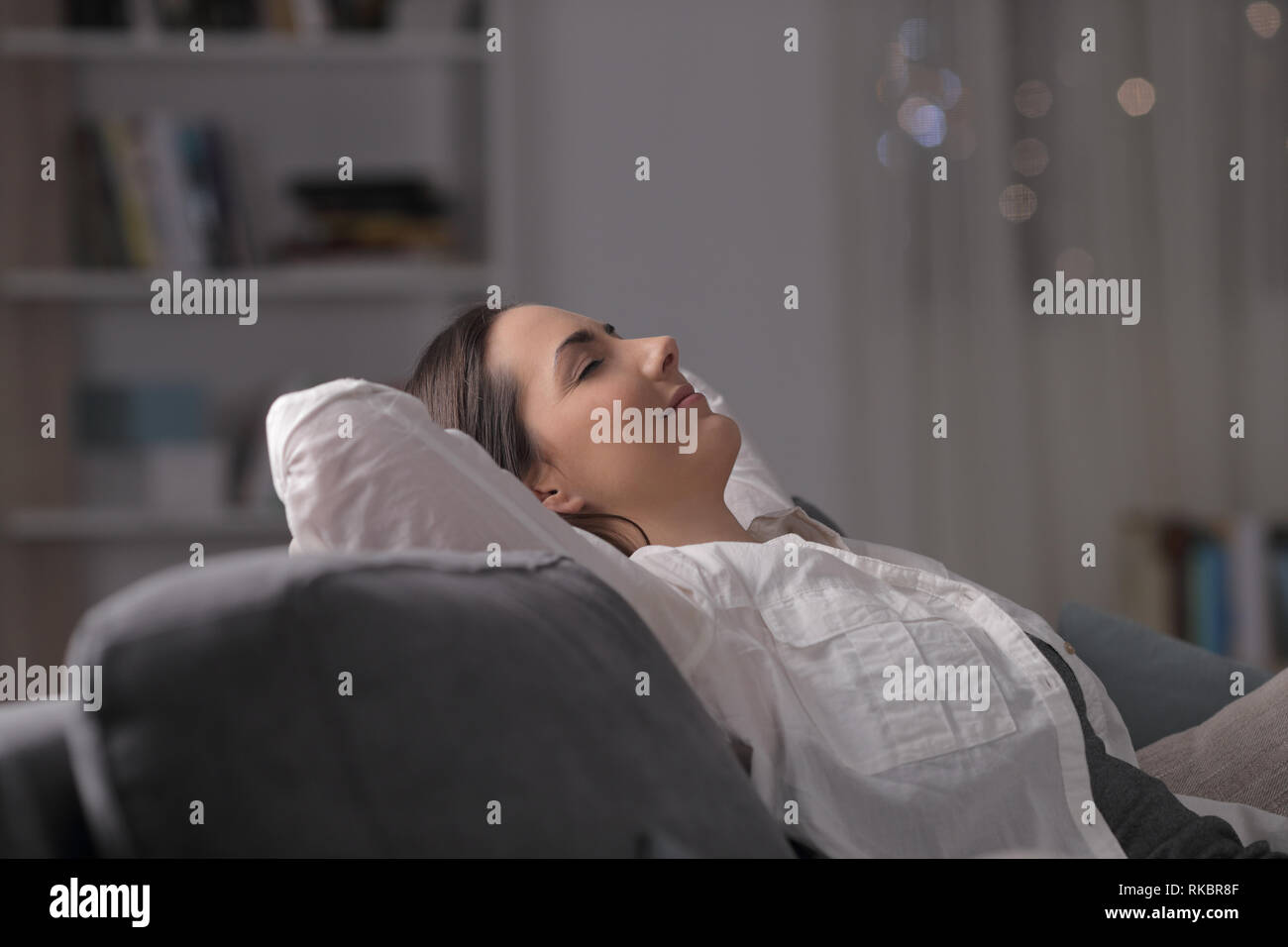 Vista laterale ritratto di una donna appoggiato comodamente seduto su un divano nella notte a casa Foto Stock
