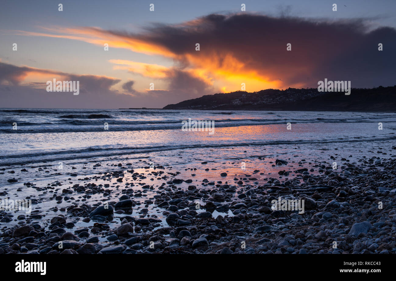 Charmouth, Dorset, Regno Unito. Il 10 febbraio 2019. Regno Unito: Meteo La moody cieli serali presso Charmouth sono accesi con vibrante colore arancione al tramonto di domenica sera. A seguito di un fine settimana di forti venti e piogge hanno portato dalla tempesta Erik un periodo di calma e più si stabilirono Meteo previsioni per il sud ovest di questa settimana. Credito: PQ/Alamy Live News Foto Stock