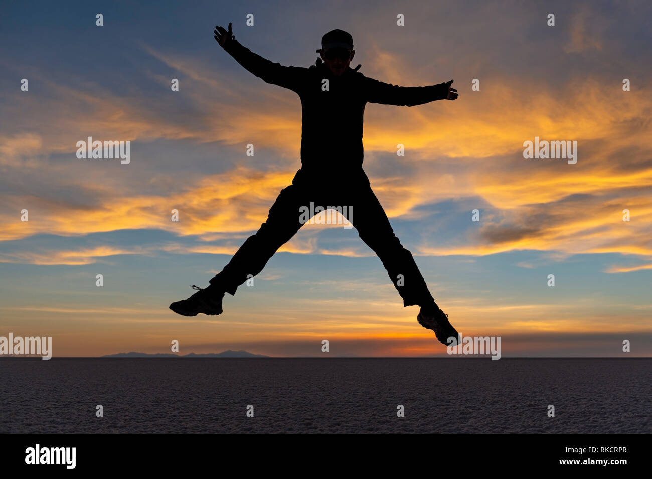 Jump shot con la silhouette di un uomo giovane e turisti in sale di Uyuni piatto (Salar de Uyuni) al tramonto, Bolivia. Foto Stock