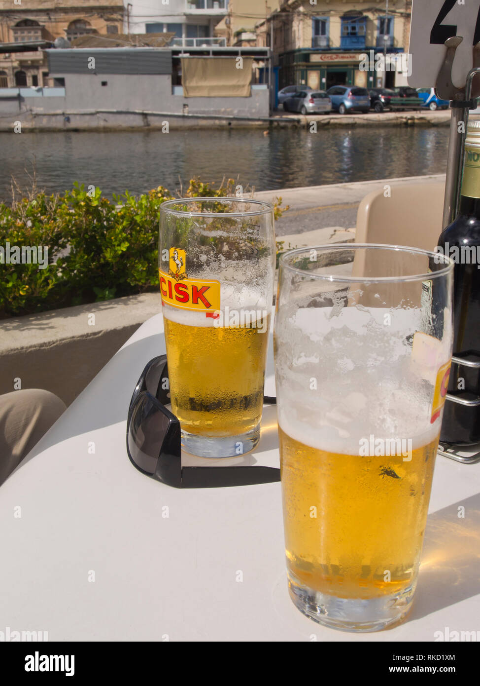 Mezzo pieno o vuoto bicchieri di birra Cisk su un tavolo all'aperto al sole, vacanza a Malta nei pressi di La Valletta Foto Stock